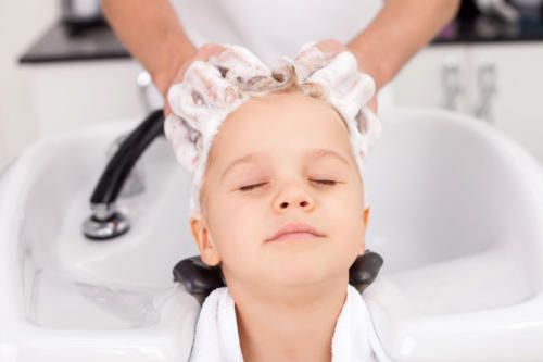 Skilled young hairdresser is treating hair of child